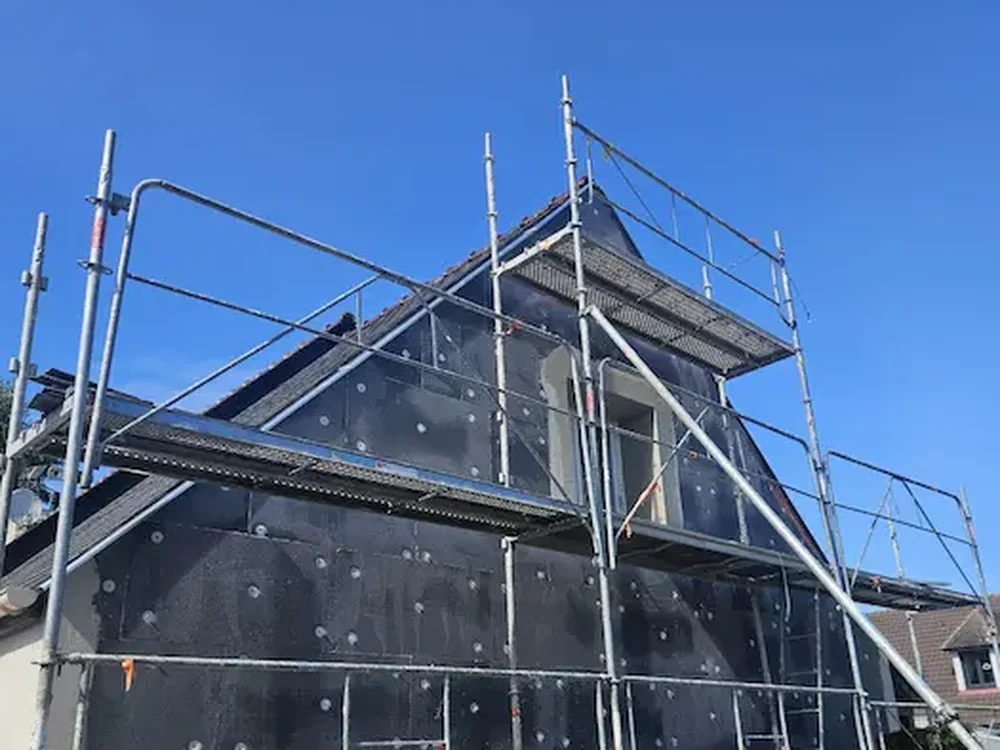 Façade d'une maison sous échafaudage avec protection lors d'une isolation thermique par l'extérieur dans le Calvados